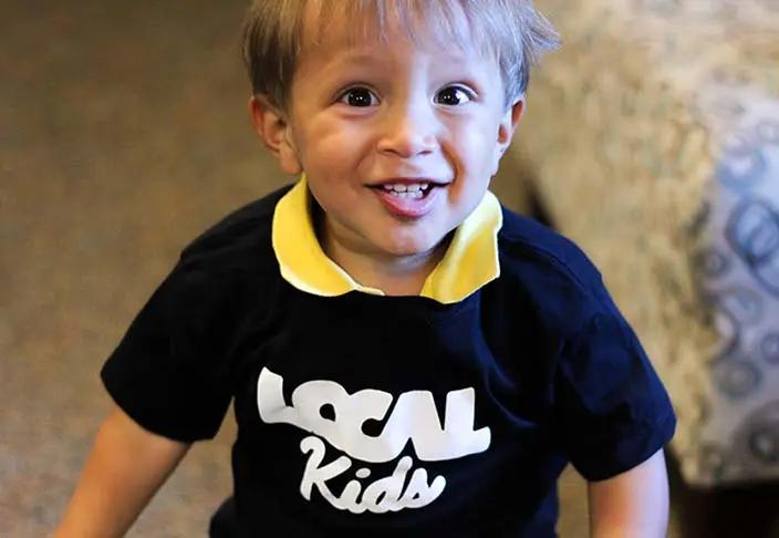 A picture of a smiling child in a 'Local Kids' shirt